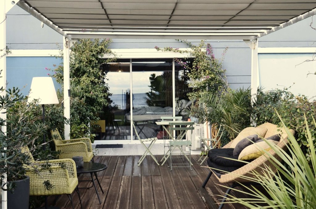 Outdoor area with plants, chairs, and pergola next to a blue house